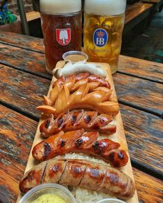 a wooden table topped with hot dogs and french fries next to two beer mugs