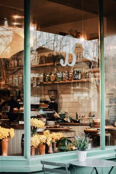 the window of a bakery with flowers in pots and potted plants on the table