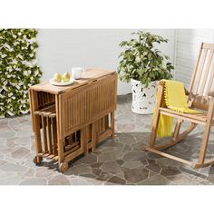 a wooden rocking chair next to a table with fruit on it and a potted plant