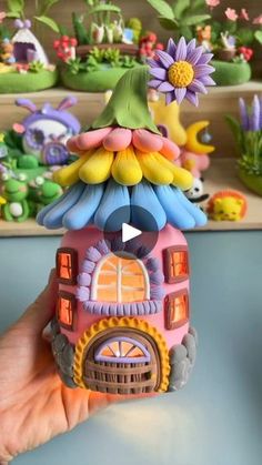 a hand holding a small toy house in front of some fake flowers and other toys