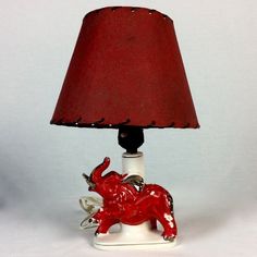 a red elephant lamp sitting on top of a white table next to a red shade