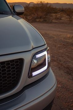 the front end of a silver car with its lights on at sunset in the desert