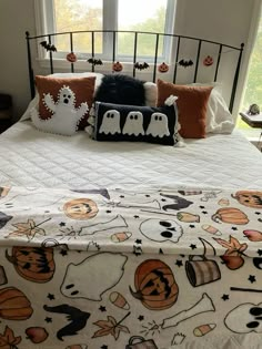 a bed with halloween pillows on it in front of a window and pumpkins hanging from the headboard