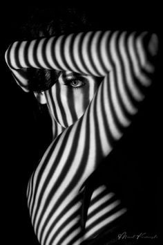 a woman's face is covered by the shadow of a striped curtain in black and white