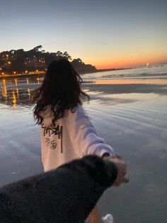 a woman walking on the beach carrying a surfboard at sunset with her arm in the air