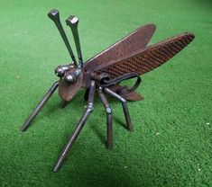 a metal insect sitting on top of a green floor covered in lots of screws