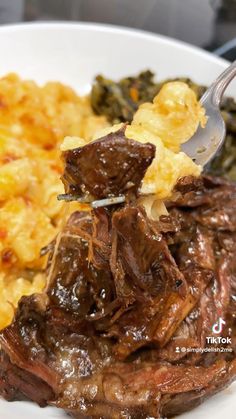 a fork is stuck into some meat and vegetables on a plate with macaroni and cheese