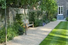 a garden area with a bench, grass and trees in front of a brick building