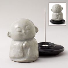 a small white buddha statue next to a black candle holder with a stick sticking out of it