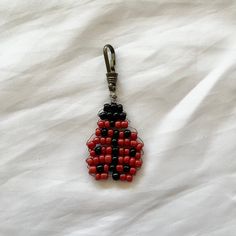 a red and black beaded keychain hanging from a metal hook on a white sheet