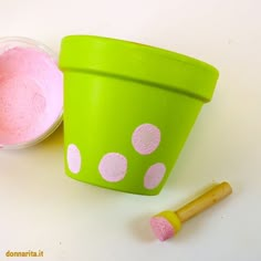 a green cup with pink paint next to a wooden stick