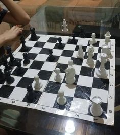 two people playing chess in front of a glass table with white and black pieces on it