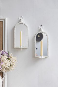 two white candle holders on the wall with flowers in vases next to one another