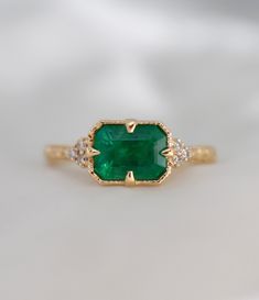 an emerald and diamond ring on a white surface