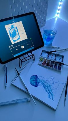 a tablet computer sitting on top of a table next to some pens and ink bottles