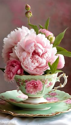 pink peonies are in a teacup on a saucer with matching plates