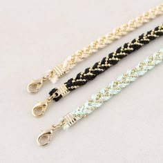 three different types of bracelets on a white surface with gold and black cords,