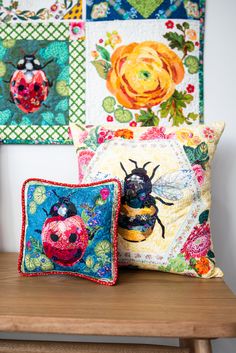 two decorative pillows sitting on top of a wooden bench in front of wall hangings