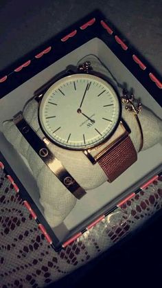 a watch sitting in a box on top of a lace covered table cloth with red and white trim