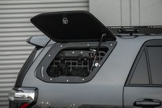 an open trunk on the back of a gray car in front of a garage door