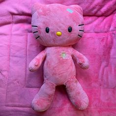 a pink hello kitty stuffed animal laying on top of a pink bed sheet with the word hello kitty written on it