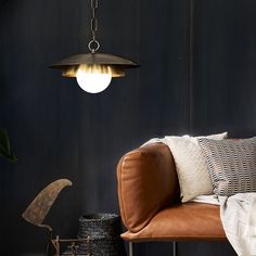 a living room with a brown leather couch and black wall behind it, hanging light fixture