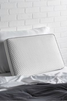 a white pillow sitting on top of a bed next to a brick wall and pillows