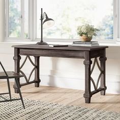 a wooden desk with a lamp on it next to a chair in front of a window