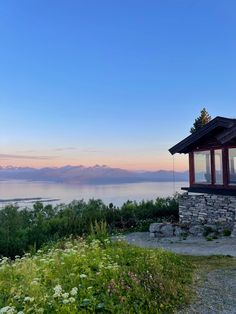 a small cabin sitting on top of a hill next to the ocean with mountains in the background