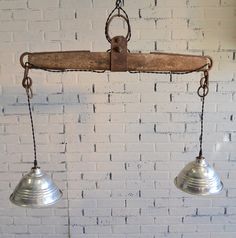 two metal bells hanging from a brick wall next to a light fixture on a chain