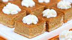 four pieces of pumpkin cheesecake on a white square plate with whipped cream toppings