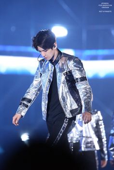 a male in a silver jacket and black pants on stage with his hand out to the side