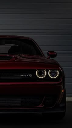 the front end of a red sports car in a dark garage with its lights on