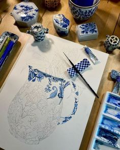 a table topped with lots of blue and white vases next to paintbrushes