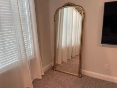 a large gold framed mirror sitting in front of a window next to a white curtain