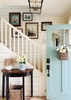 a blue door is next to a table with flowers and baskets on it in front of the stairs