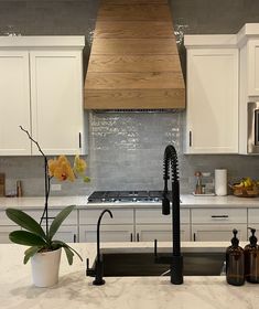 a kitchen with white cabinets and marble countertops has a black faucet in the center