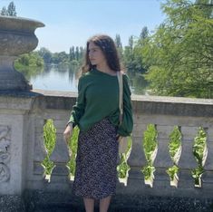 a woman standing in front of a stone wall next to a body of water and trees