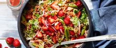 a bowl filled with strawberries and salad next to two spoons on a table