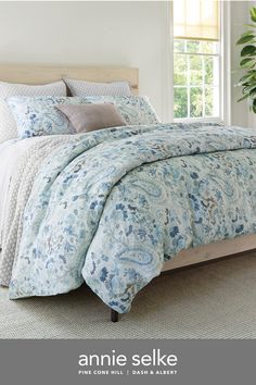 a bed with blue and white comforters in a bedroom next to a plant on the floor