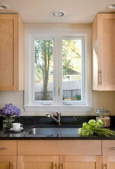 a kitchen with wooden cabinets and black granite counter tops next to a window that looks out onto the backyard