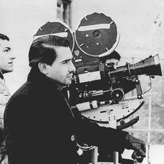 black and white photograph of two men looking at an old movie projector on a tripod