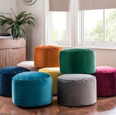 four different colored stools sitting on top of a wooden floor next to a window