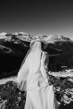 a woman wearing a veil and hat standing on top of a snow covered mountain