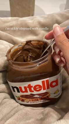 a hand holding a spoon over a jar of nutella on a bed with the words nutella written above it