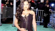 a woman in a black corset posing for the camera at a green carpet event