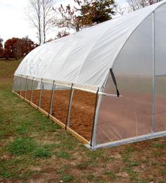 a small greenhouse in the middle of a field with grass and dirt growing inside it