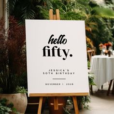 a sign that says hello fifty sits in front of a table with flowers and greenery