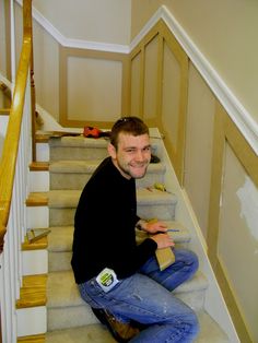 a man is sitting on the stairs in his house smiling at the camera and holding a paint roller