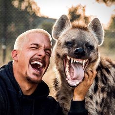 a man is holding a hyena up to his face with it's mouth open